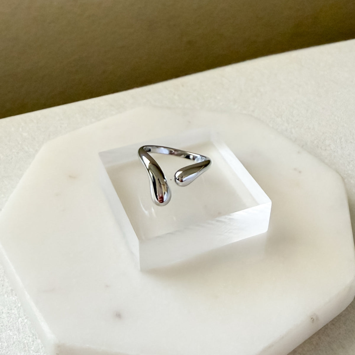 Silver ring on a white stone surface with a neutral background  Liquid Curve Ring - The Songbird Collection