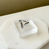 Silver ring on a white stone surface with a neutral background  Liquid Curve Ring - The Songbird Collection