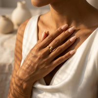 Person wearing a gold ring with a blurred background of ceramic vases. Liquid Curve Ring - The Songbird Collection