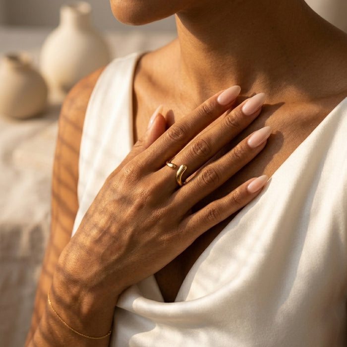 Person wearing a gold ring with a blurred background of ceramic vases. Liquid Curve Ring - The Songbird Collection
