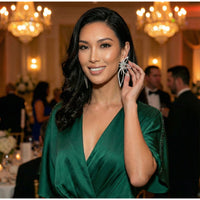 Woman wearing a green dress and large floral petal shaped rhinestone statement earrings in an elegant indoor setting