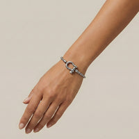 Silver bracelet on a person's wrist against a beige background Lucky_Shackle_Bracelet_stainless_steel_The_Songbird_Collection