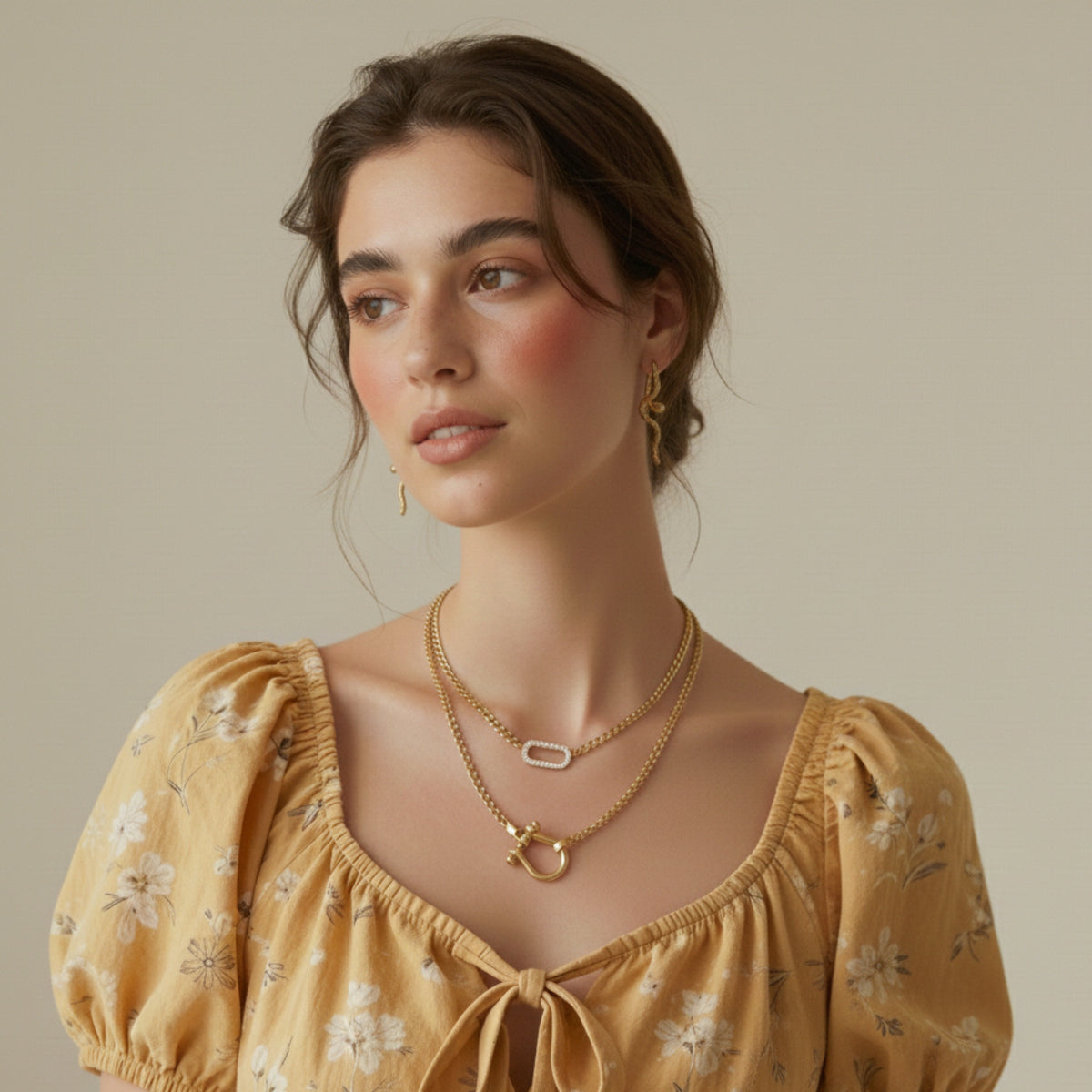 Woman wearing a yellow floral dress and gold horseshoe shaped chain link necklace and a micro pave link necklace with gold snake earrings.
