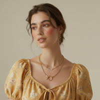 Woman wearing a yellow floral dress and gold horseshoe shaped chain link necklace and a micro pave link necklace with gold snake earrings.