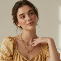 Woman wearing a yellow floral dress and gold horseshoe shaped chain link necklace and a micro pave link necklace with gold snake earrings.