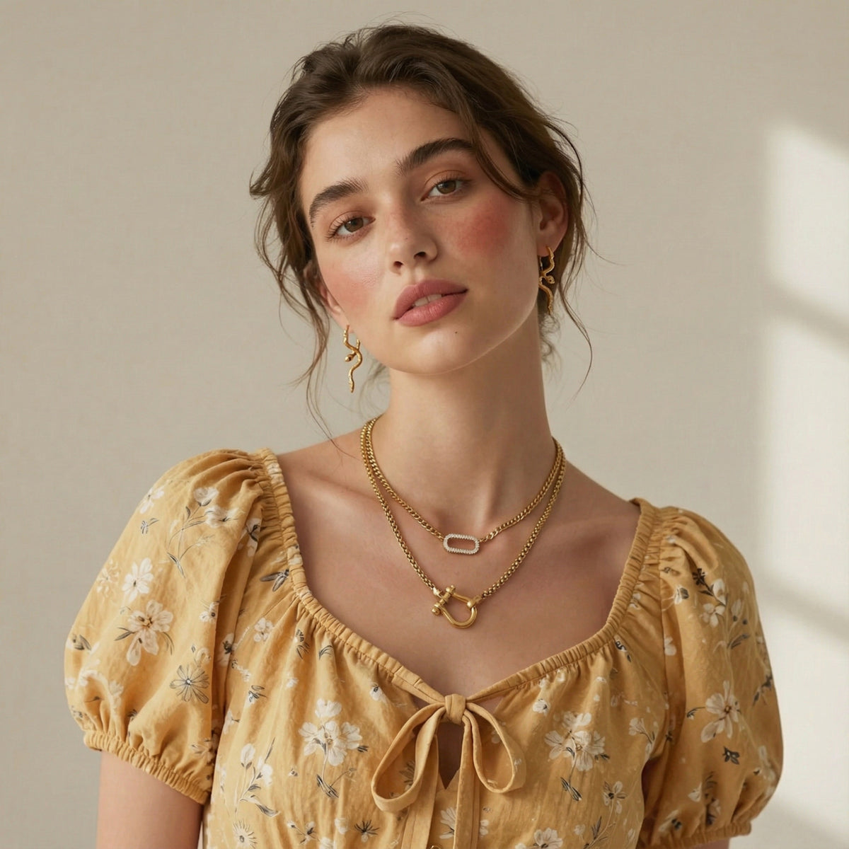 Woman wearing a yellow floral dress and gold horseshoe shaped chain link necklace and a micro pave link necklace with gold snake earrings.