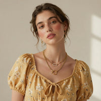 Woman wearing a yellow floral dress and gold horseshoe shaped chain link necklace and a micro pave link necklace with gold snake earrings.