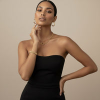 Woman wearing horseshoe shaped necklace and watch chain link bracelet gold jewelry against a beige - The Songbird Collection