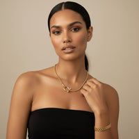 Woman wearing horseshoe shaped necklace and watch chain link bracelet gold jewelry against a beige 