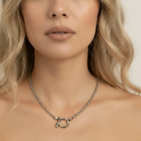 Close-up of a woman wearing a silver necklace with a horsebit clasp.