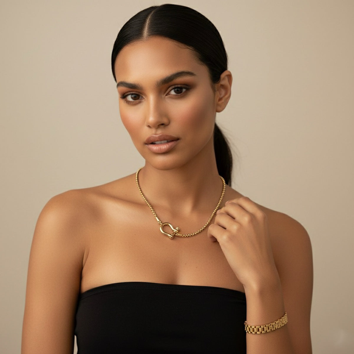 Woman wearing a horse shoe shaped gold necklace and bracelet against a beige background