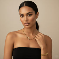 Woman wearing a horse shoe shaped gold necklace and bracelet against a beige background