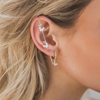 A person wearing a gold-plated copper ear cuff and earrings featuring butterfly designs with cubic zirconia.