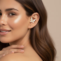 Woman wearing a delicate leaf-shaped  or butterfly shaped ear cuff ear stick ear hook earring with a neutral background
