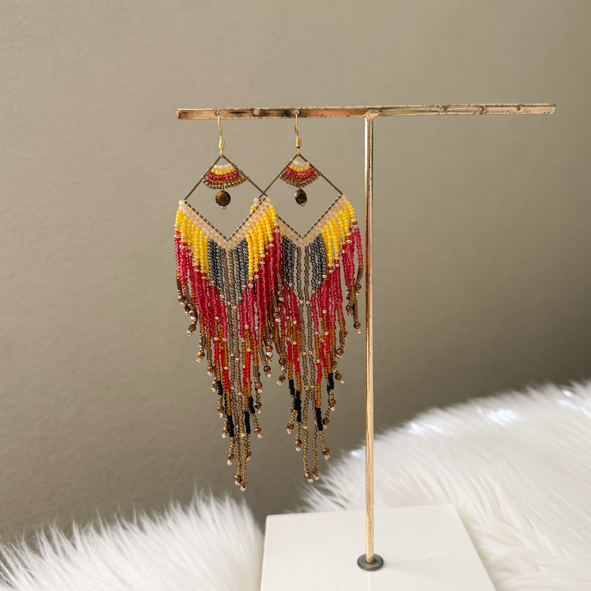 Multicolored beaded earrings on a gold stand against a neutral background