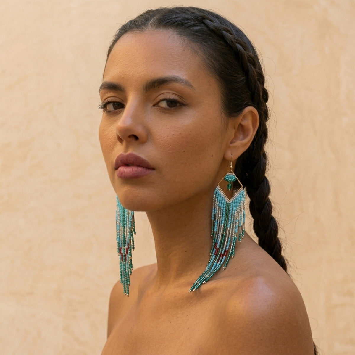 Woman wearing turquoise beaded earrings against a beige background