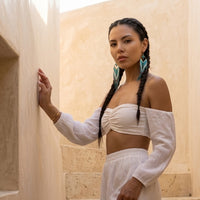 Woman in a white outfit standing against a beige stone wall.