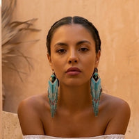 Woman wearing large turquoise earrings against a beige background