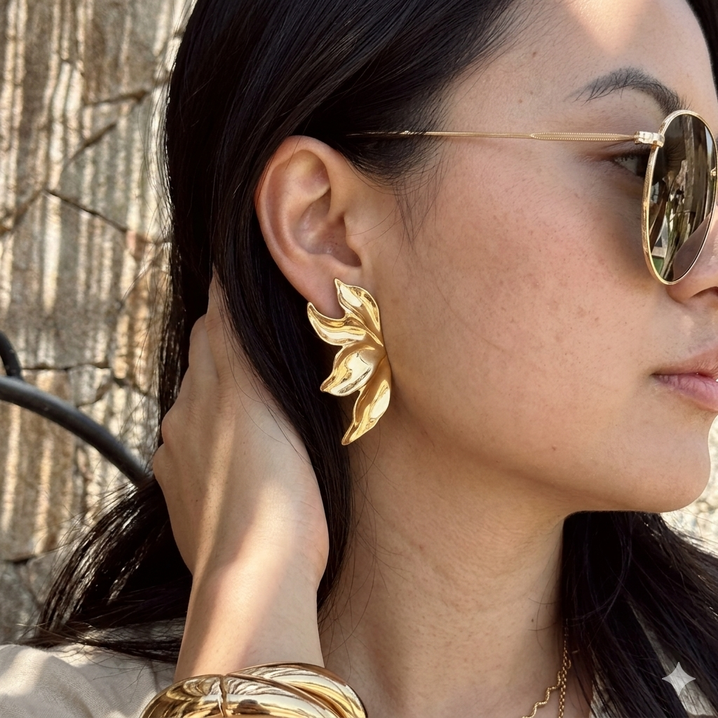 Woman wearing gold earrings and sunglasses with a textured wall background. Molten Flame Statement Earrings - The Songbird Collection