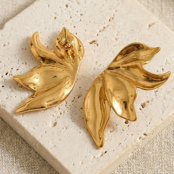 Gold leaf-shaped earrings on a textured beige surface. Molten Flame Statement Earrings - The Songbird Collection 