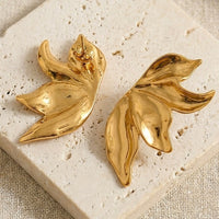 Gold leaf-shaped earrings on a textured beige surface. Molten Flame Statement Earrings - The Songbird Collection 