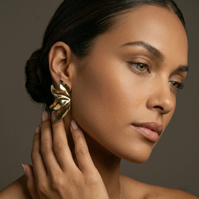 Woman wearing a gold leaf earring against a neutral background. Molten Flame Statement Earrings - The Songbird Collection