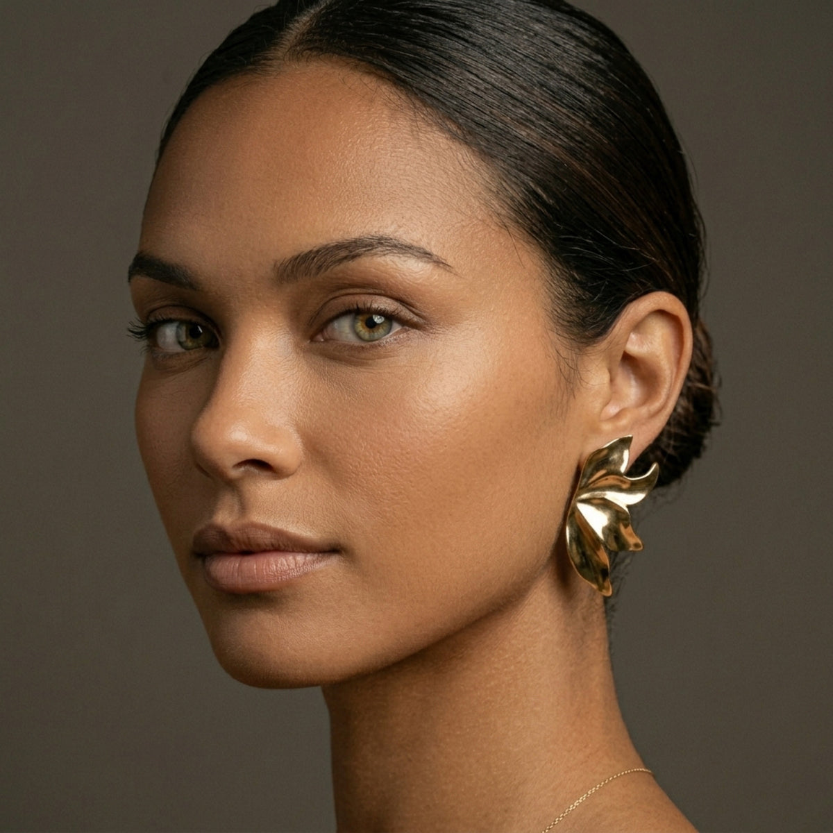 Woman wearing gold earrings against a neutral background. Molten Flame Statement Earrings - The Songbird Collection