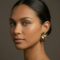 Woman wearing gold earrings against a neutral background. Molten Flame Statement Earrings - The Songbird Collection