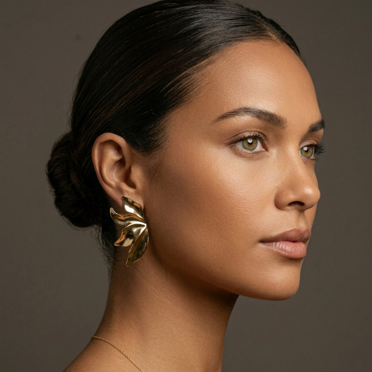 Woman wearing gold earrings against a brown background. Molten Flame Statement Earrings - The Songbird Collection