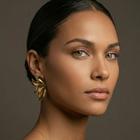 Close-up of a woman wearing a gold earring against a neutral background. Molten Flame Statement Earrings - The Songbird Collection