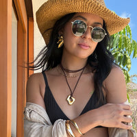 Woman wearing a straw hat, sunglasses, and gold jewelry outdoors.  Molten Flame Statement Earrings - The Songbird Collection