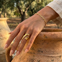Hand wearing a Molten gold Statement ring and Aura Ripple bracelet on a rustic background