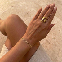 Gold bracelet and ring on a hand against a neutral background. Molten Gold Statement Ring - The Songbird Collection