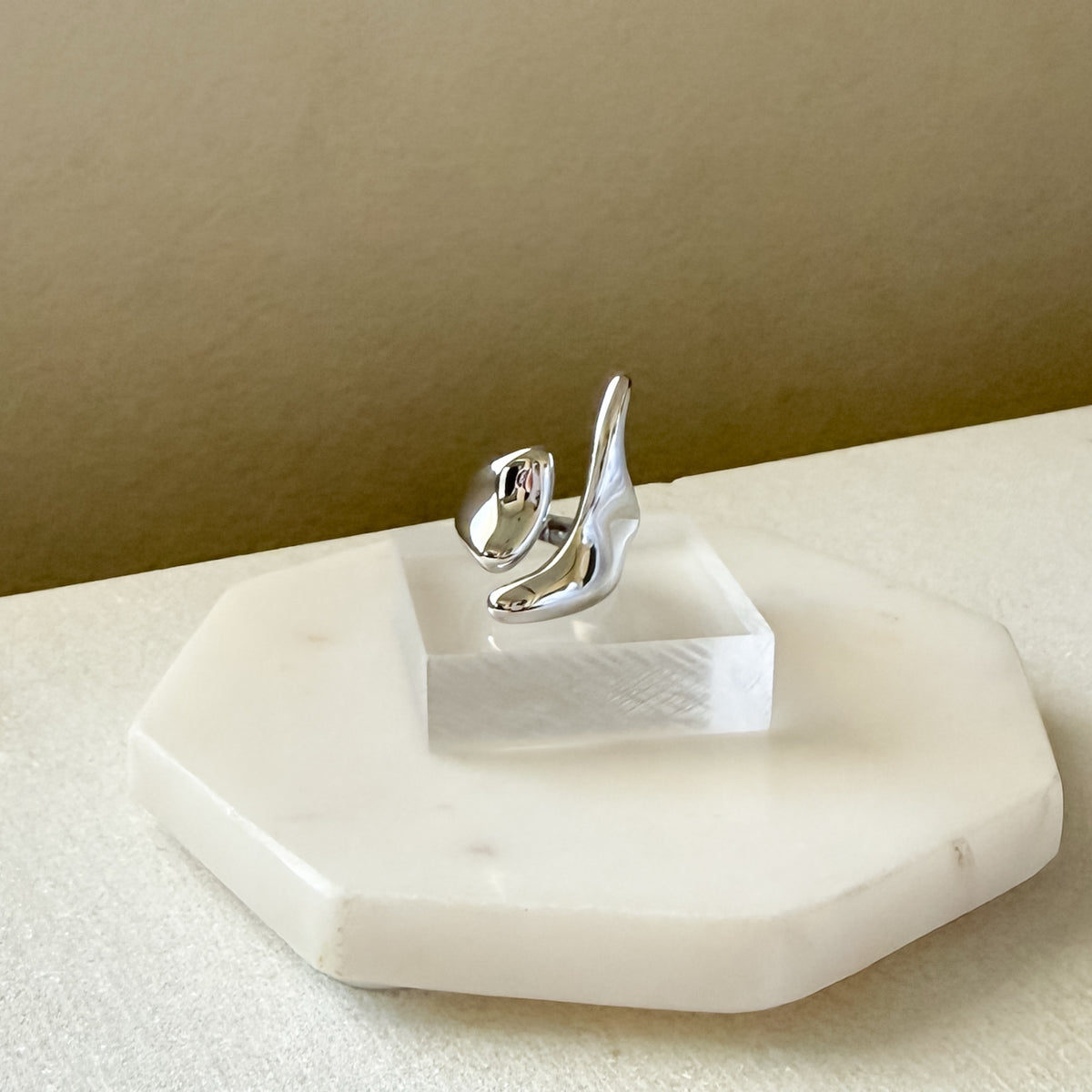 Silver ring on a hexagonal marble stand against a beige background. Molten Gold Statement Ring - The Songbird Collection