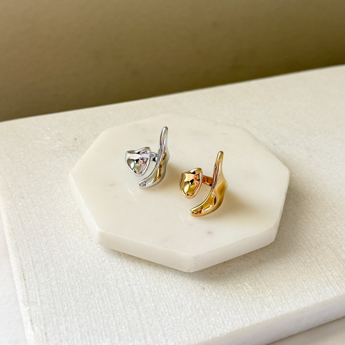 Gold and silver earrings on a white stone surface with a beige background. Molten Gold Statement Ring - The Songbird Collection
