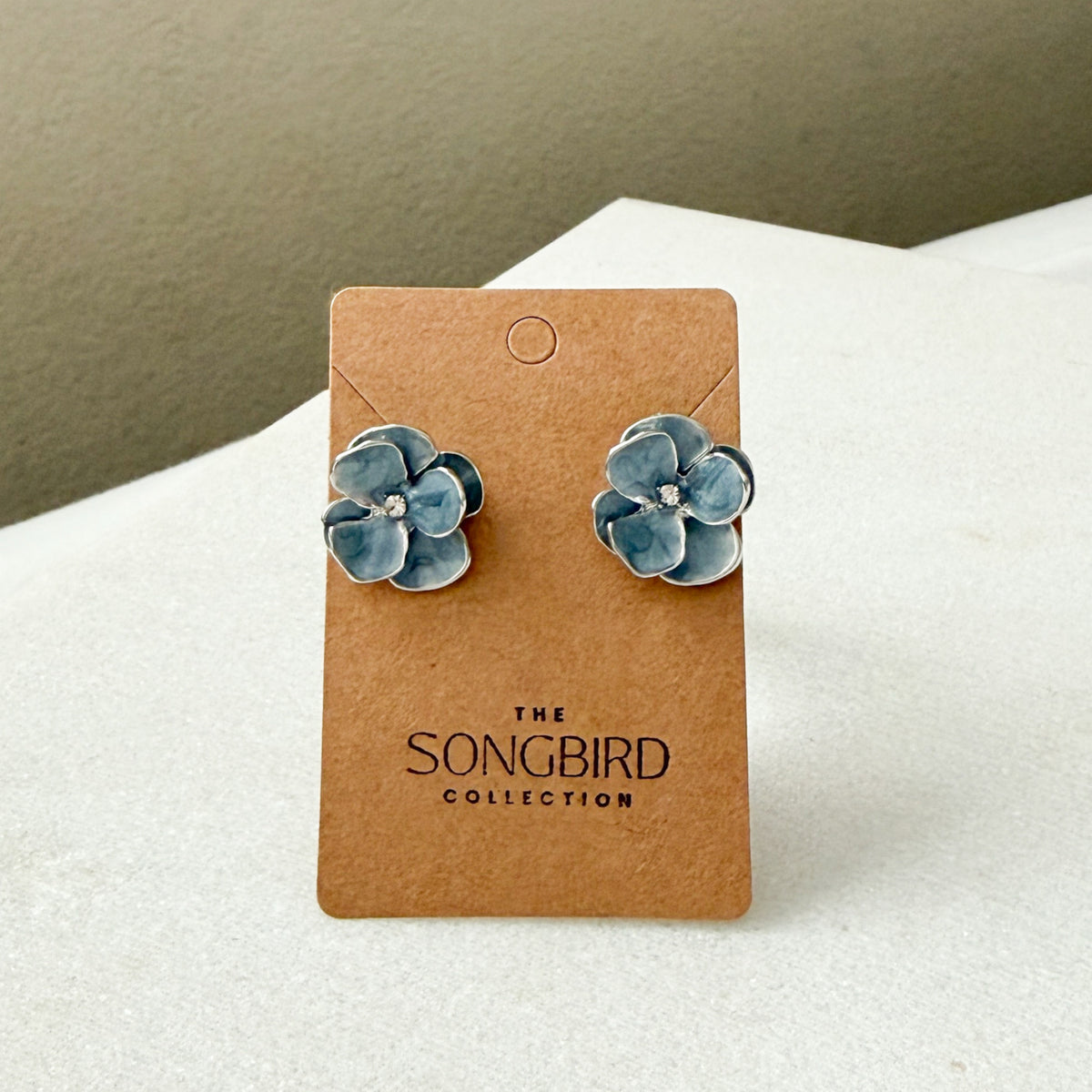 Blue flower earrings on a brown card with 'The Songbird Collection' branding.