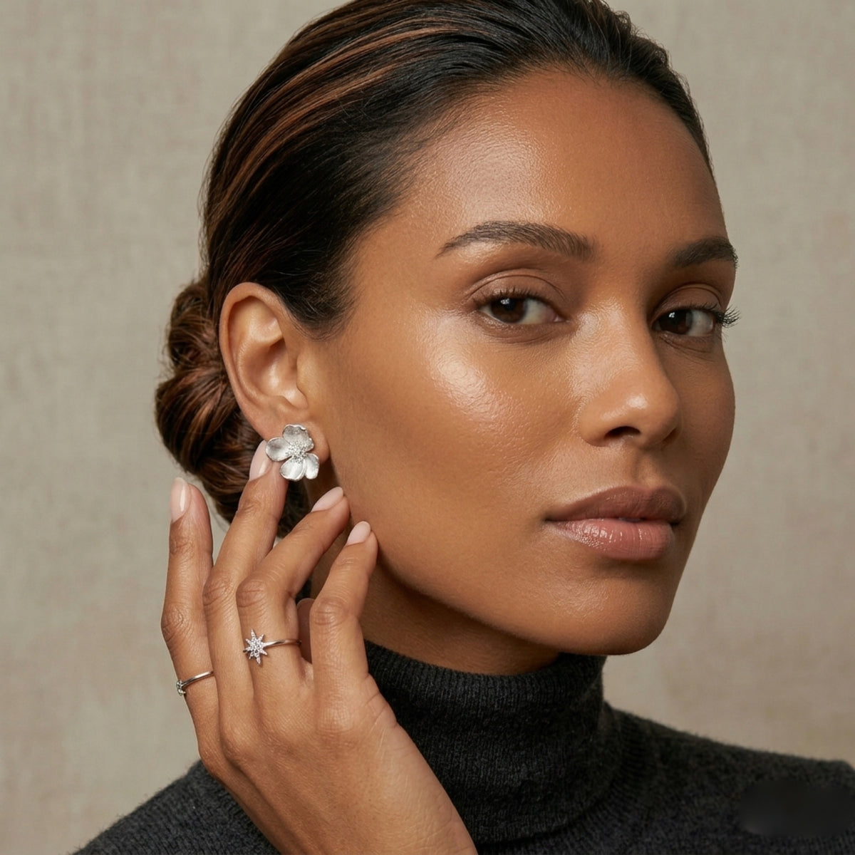 Woman wearing a floral earring and ring against a neutral background