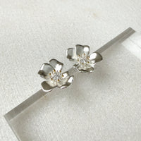 Silver flower-shaped earrings with clear gemstones on a white background