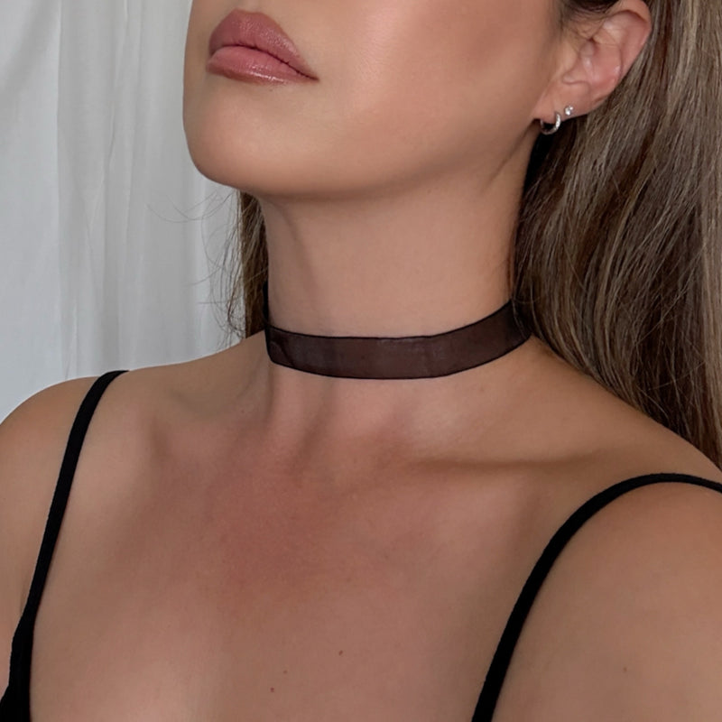 Close-up of a woman wearing a black choker necklace against a neutral background