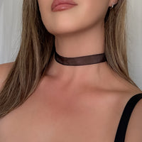 Close-up of a person wearing a black choker necklace with a neutral background