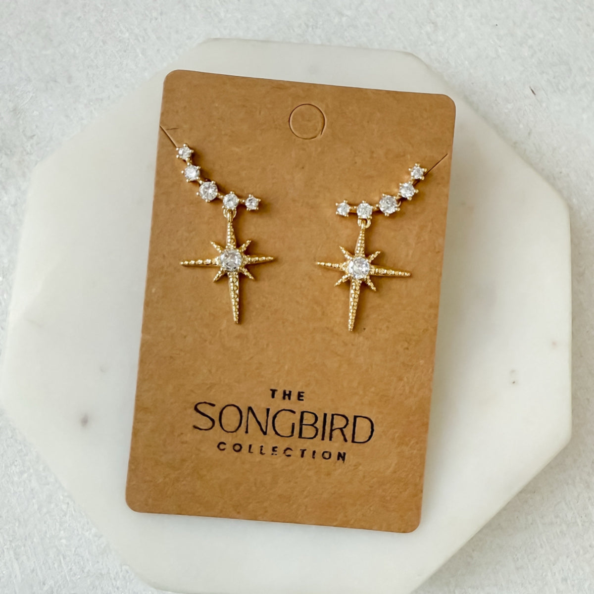 Star-shaped earrings on a 'The Songbird Collection' card against a white background