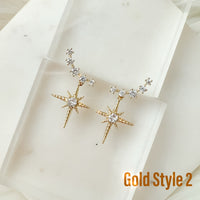 A pair of gold-colored ear crawlers with cubic zirconia and a star drop pendant, displayed on a fabric surface.