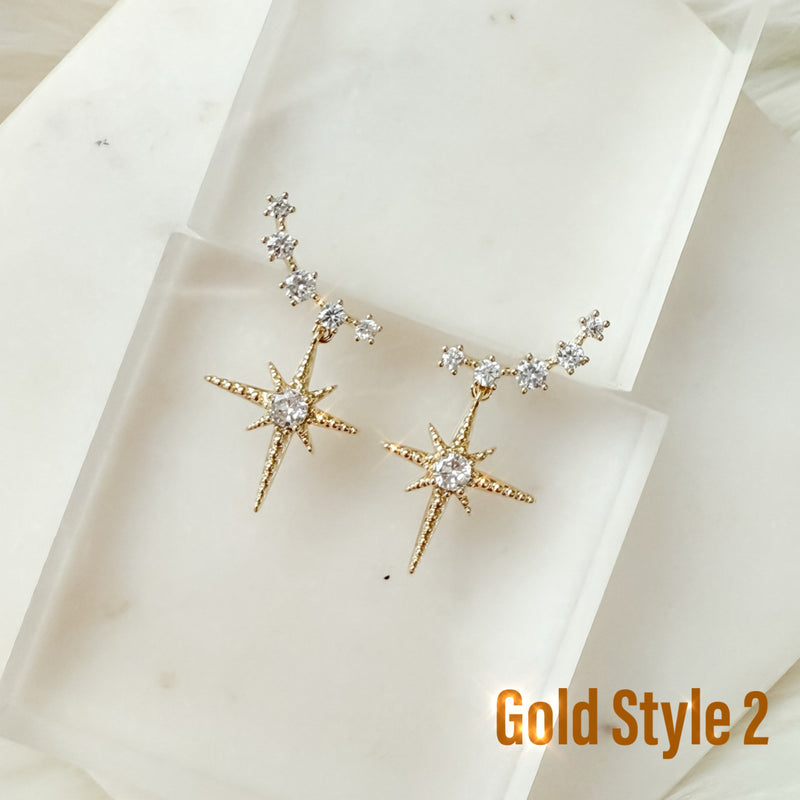 A pair of gold-colored ear crawlers with cubic zirconia and a star drop pendant, displayed on a fabric surface.