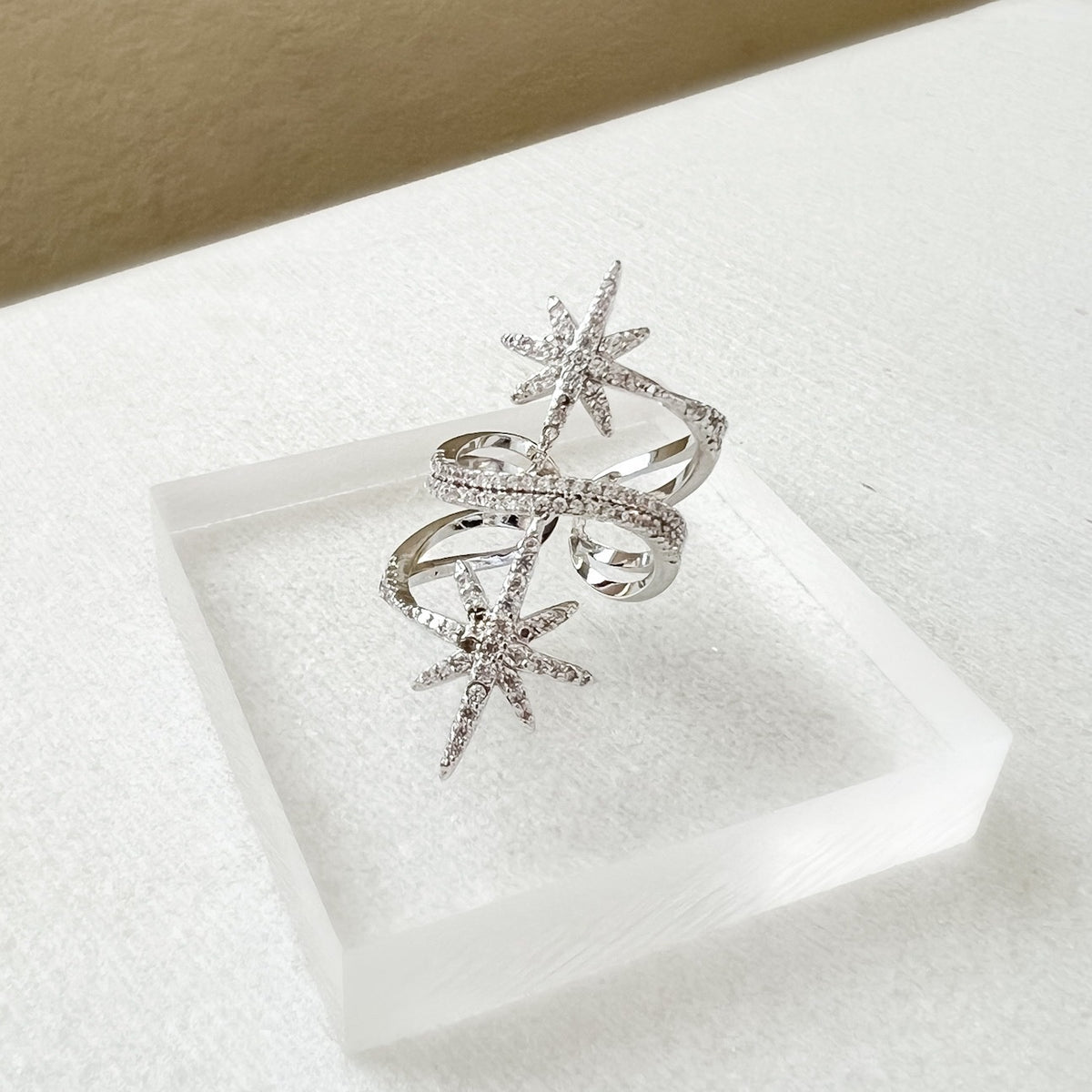 An elegant North Star statement ring with platinum plating and sparkling cubic zirconia stones displayed on a clear square platform.