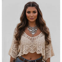 Woman wearing a beige crochet top and denim shorts with a neutral background