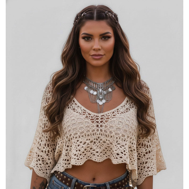 Woman wearing a beige crochet top and denim shorts with a neutral background