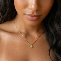A close-up of a woman wearing a delicate gold chain necklace with a small flower-shaped pendant.  Petite Petal Necklace - The Songbird Collection