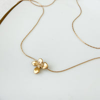 A delicate gold chain necklace featuring a small, textured gold flower pendant, displayed on a clean white surface.  Petite Petal Necklace - The Songbird Collection
