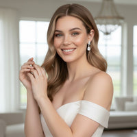Woman in a white off-shoulder dress with a blurred indoor background - bridal diamonnd drop earrings 