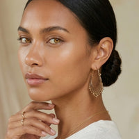 Woman wearing gold hoop earrings and a ring, with a neutral background  Priya Vintage Metal Earrings - The Songbird Collection